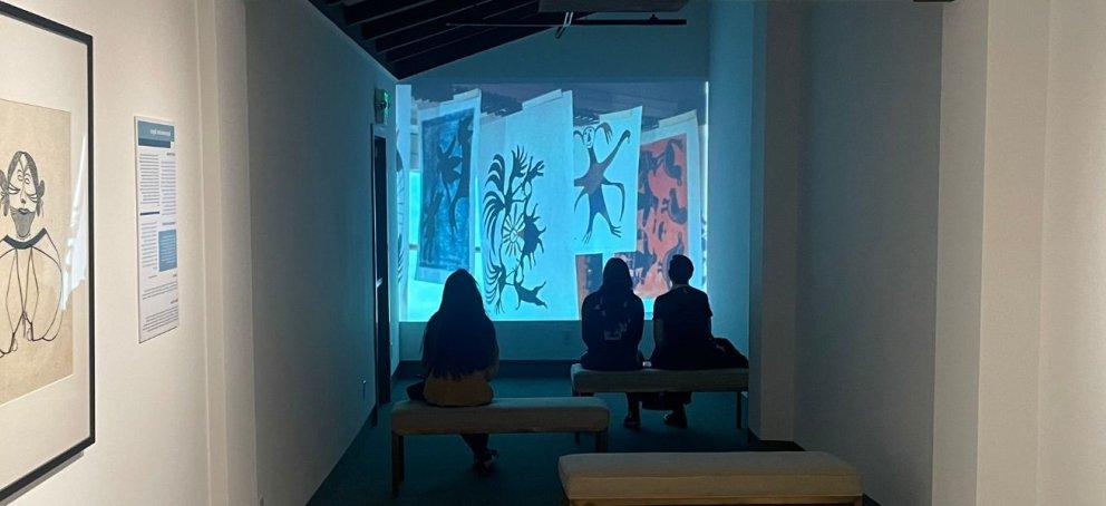 Visitors in museum gallery watching projection on wall. 